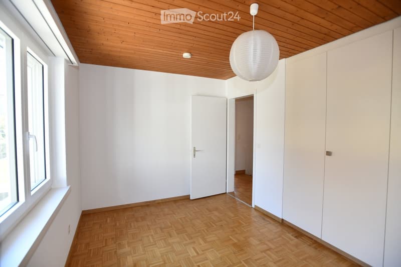 Empty room with white walls, wooden herringbone flooring, and a white pendant light fixture. Features a white door and built-in white cabinetry.