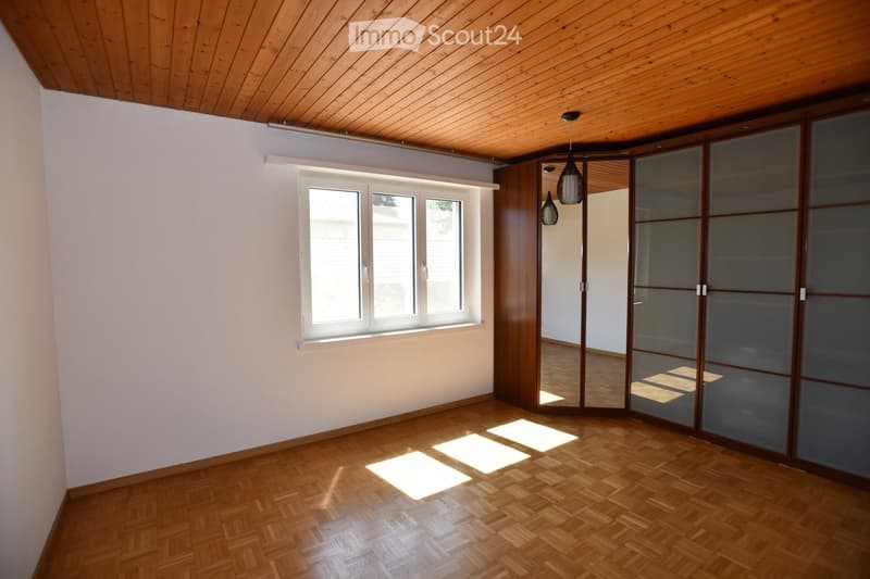 Empty room with wooden flooring, white walls, large window, and sliding glass doors leading to another space.