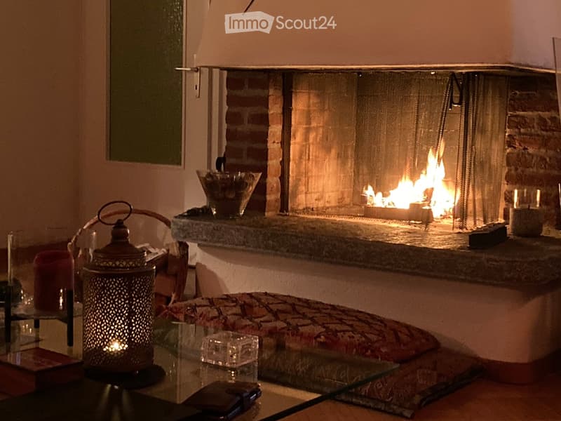 Cozy living space with a lit brick fireplace, glass coffee table, lantern, and cushioned seating area.