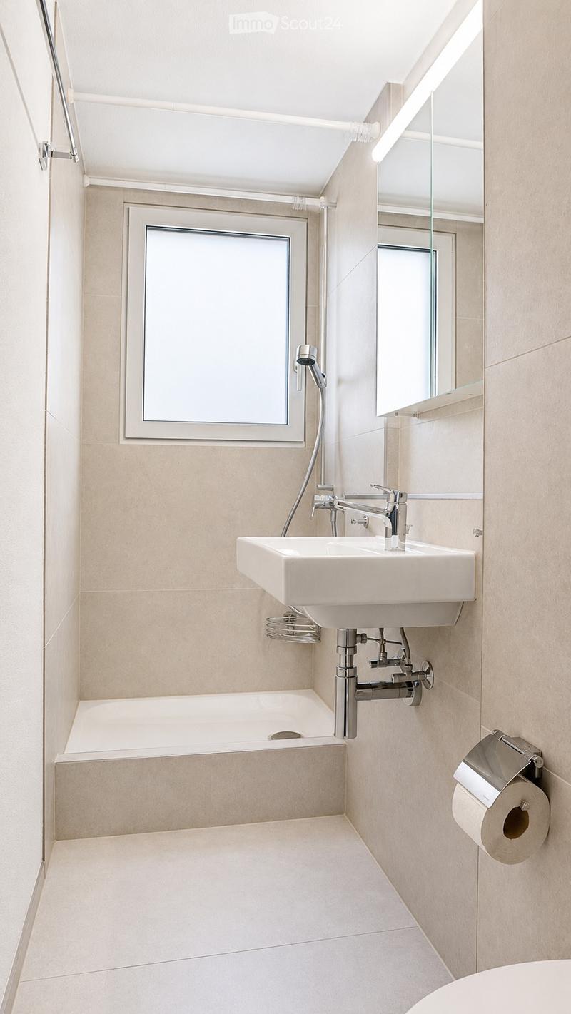 Modern bathroom with a bathtub, sink, and mirror. Light-colored tiles and sleek fixtures.