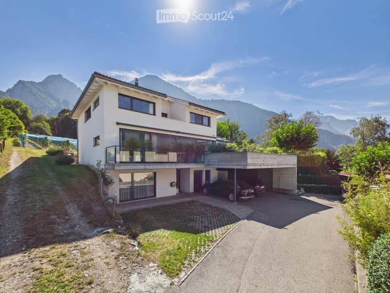 Two-story modern house with white exterior, large windows, balcony, garage, and scenic mountain view.