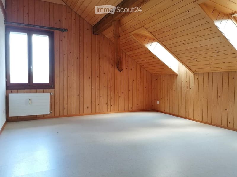 Empty attic room with wooden walls and ceiling, white floor, large window, and radiator.