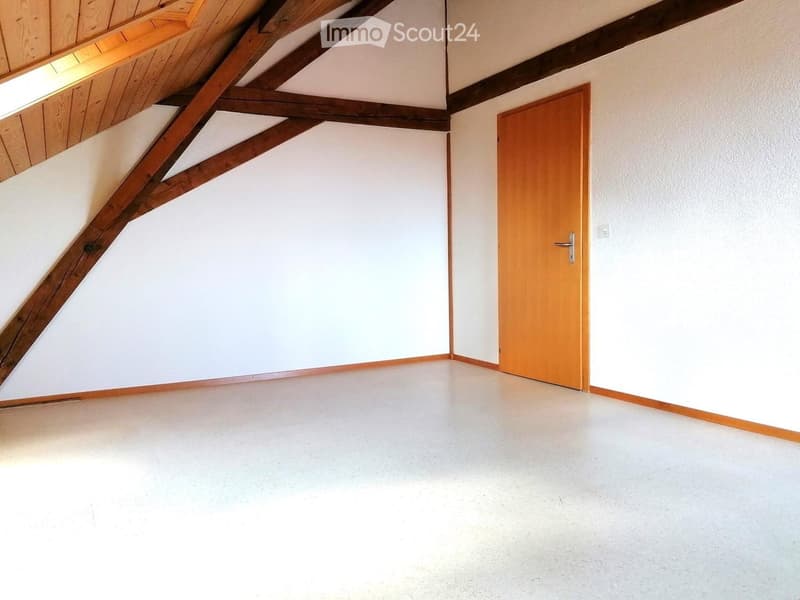 Empty attic room with wooden beams, white walls, and a single wooden door.