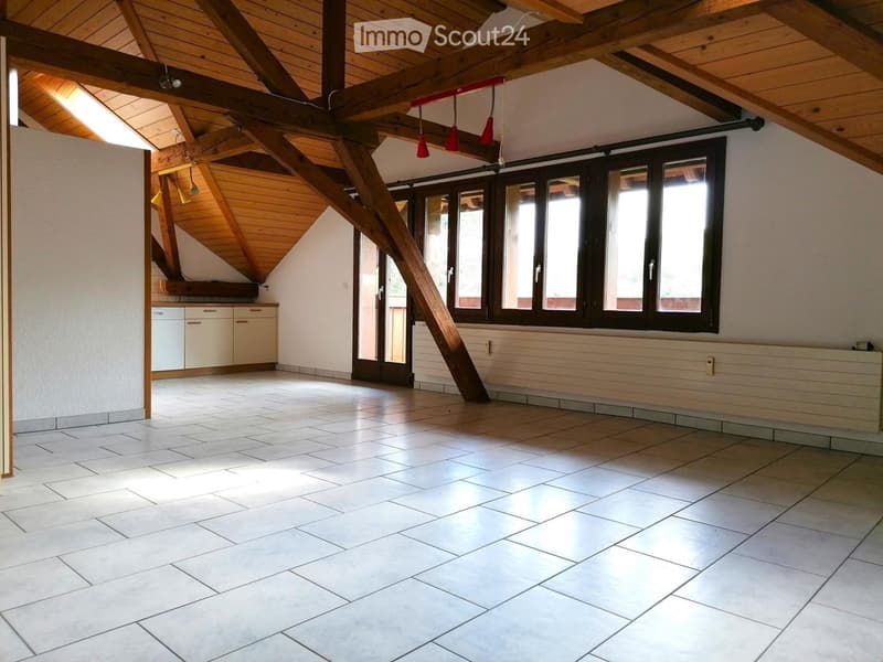Empty room with exposed wooden beams, large windows, tiled floor, and built-in cabinets.