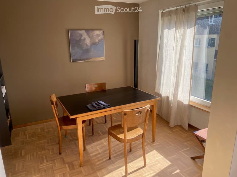 Dining room with wooden floor, dining table, chairs, and a painting on the wall.