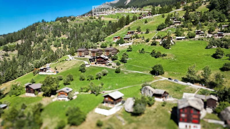 A miniature model of a village nestled in a green valley with scattered houses, trees, and winding roads.