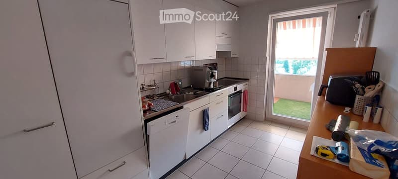 Modern kitchen with white cabinets, stainless steel appliances, and a view of the balcony. Includes a refrigerator, oven, dishwasher, sink, coffee maker, and toaster.