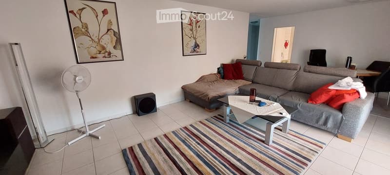 Living room with a grey sectional sofa, coffee table, fan, speaker, and a striped rug on the floor.