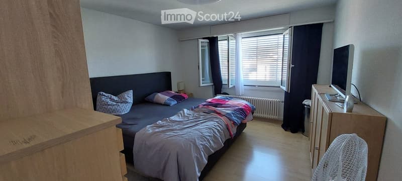Bedroom with a double bed, nightstand, fan, and a screen on a wooden cabinet.