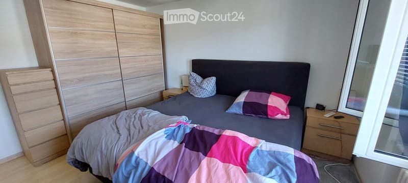 Modern bedroom with a large bed, colorful bedding, nightstands, and a wooden wardrobe.
