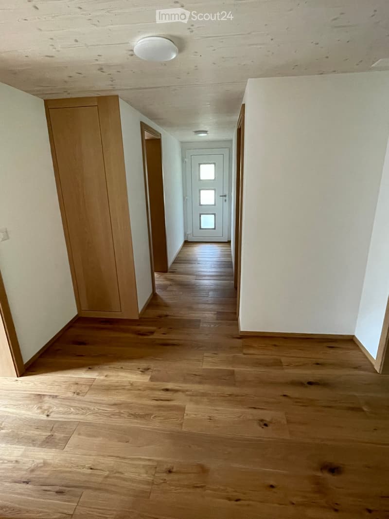 Empty hallway with wooden flooring, white walls, and a white door at the end.