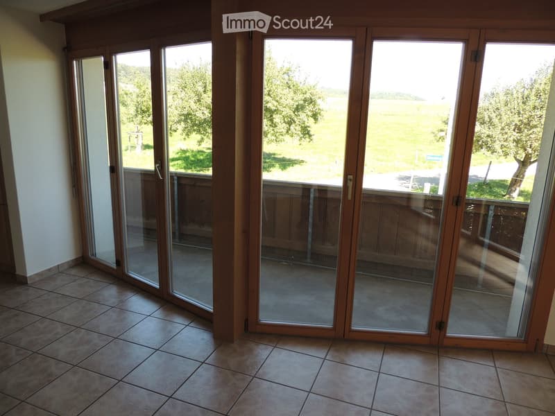 Large sliding glass doors open to a wooden deck, with a view of a green field and trees.