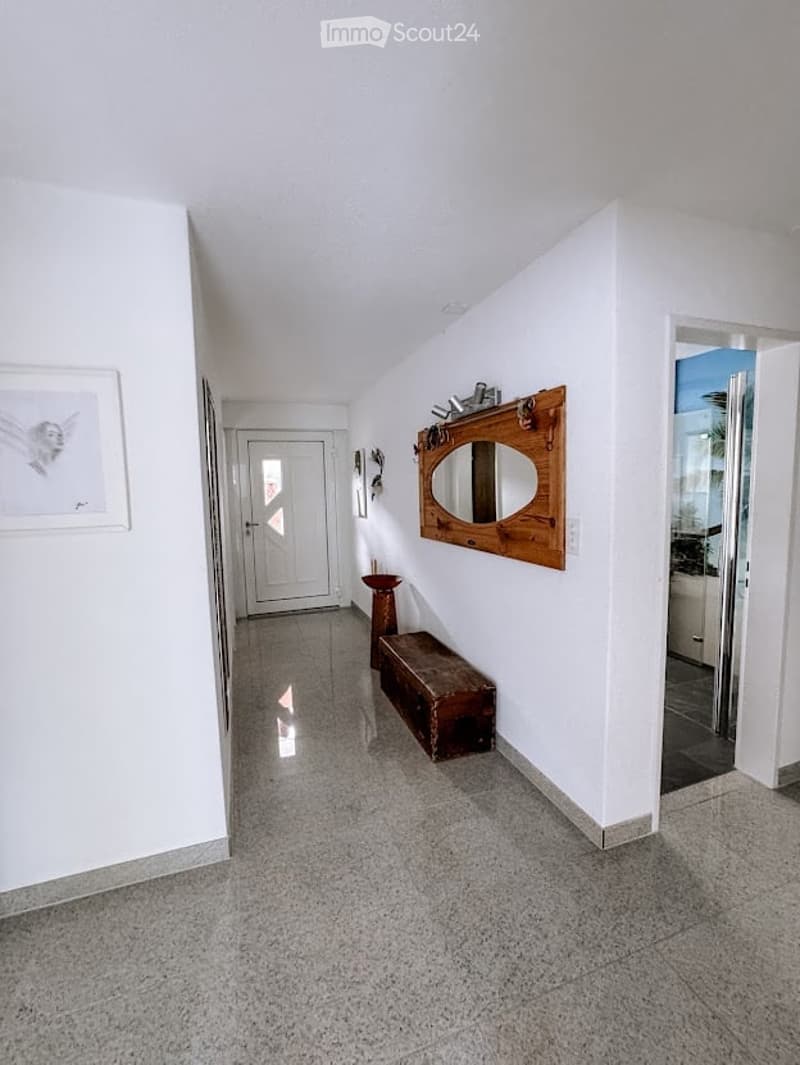 Bright hallway with white walls, tiled floor, and a wooden bench and mirror on one side.
