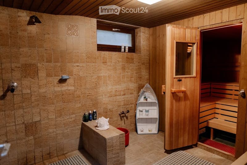 Bathroom with a shower area, wooden sauna, and a small boat-shaped shelf holding toiletries. The space features tiled walls and a wooden sauna with a mirror on the door.