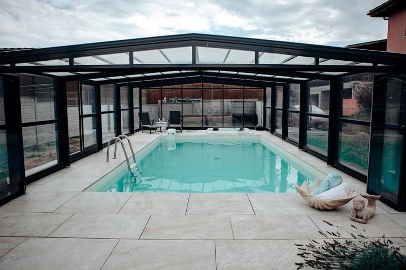 Enclosed patio with a swimming pool, lounge chairs, a small table, a hot tub, and decorative statues.