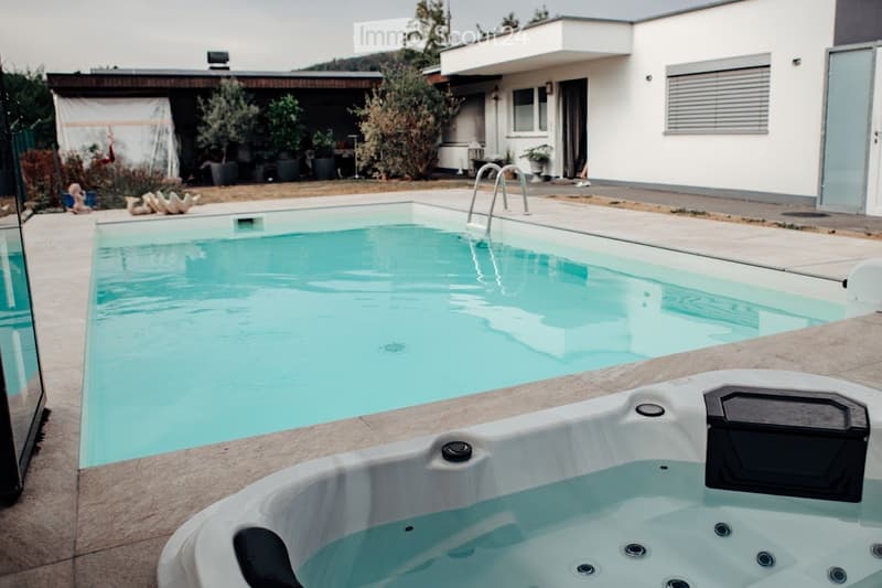 Outdoor area with a swimming pool and a hot tub, surrounded by a modern house and landscaped garden.