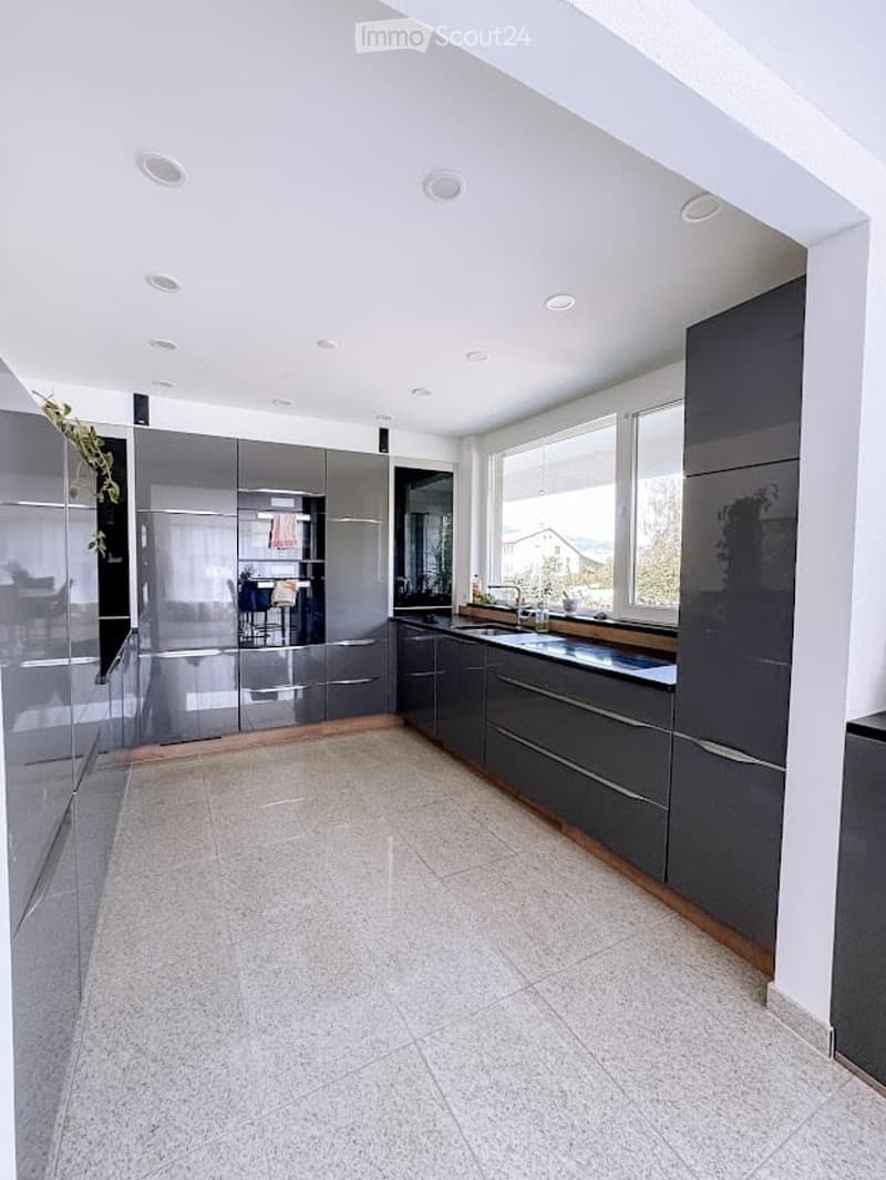 Modern kitchen with grey cabinets, white tiled floor, and large windows offering a view of the outdoors.