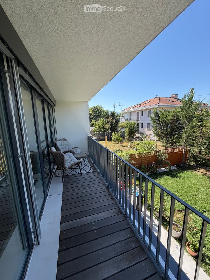 Balcony with wooden decking, metal railing, and two chairs with a small table.