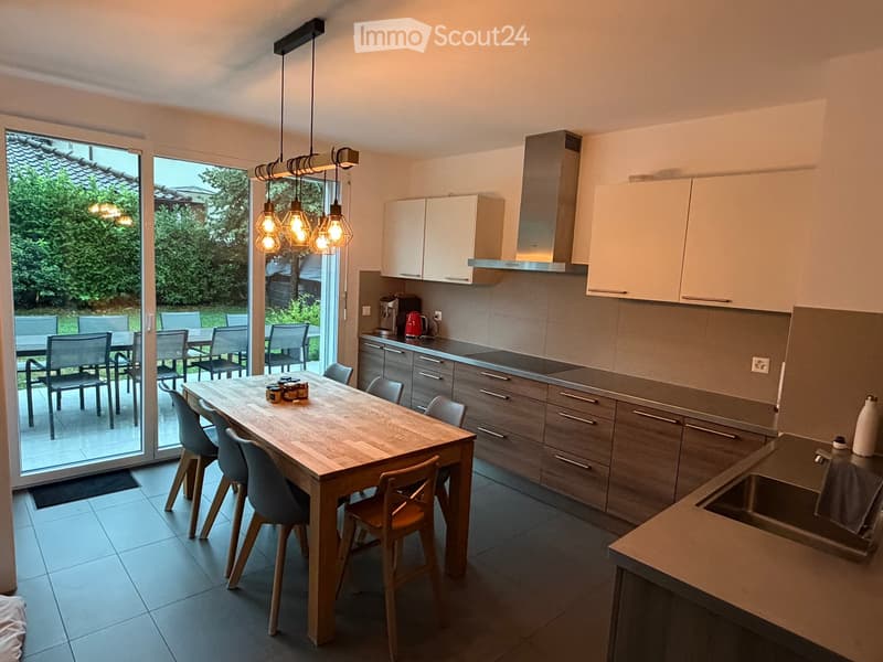 Modern kitchen with light-colored cabinets, a wooden dining table with chairs, and a large window leading to an outdoor patio.