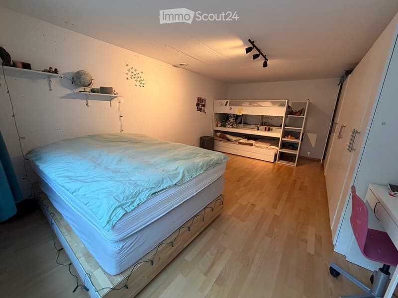 A small bedroom with a single bed, a chair, shelves, and a globe on the wall.