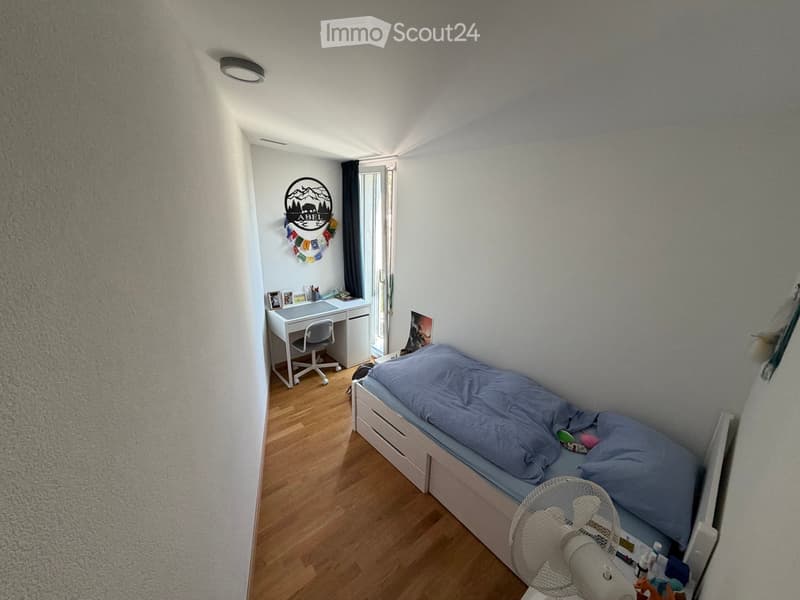 Cozy bedroom with a single bed, desk, chair, fan, and picture frame on the wall.