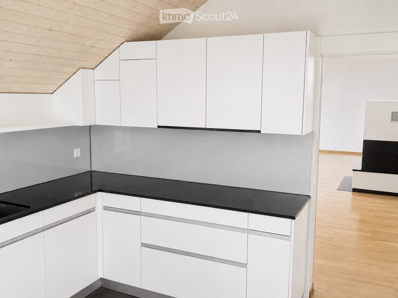 Modern kitchen with white cabinets, black countertops, and a sleek design. The space features a wooden floor and a grey backsplash.