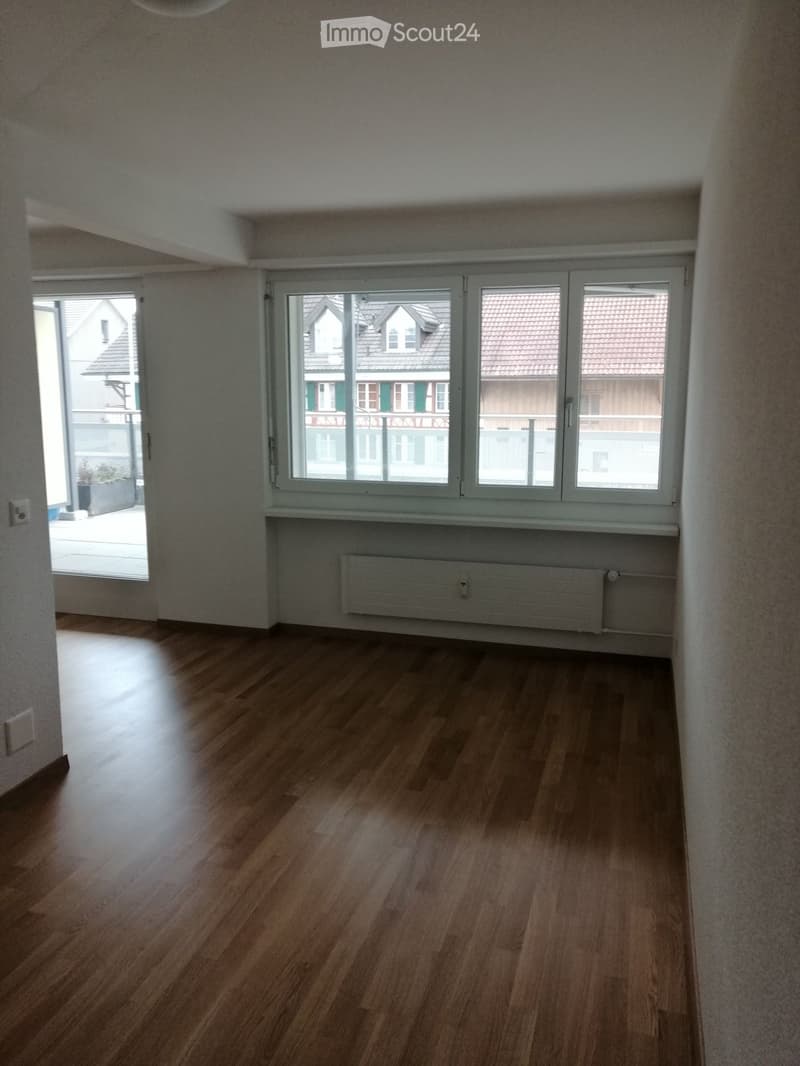 Empty room with wooden flooring, large windows, radiator, and a sliding door leading to a balcony.