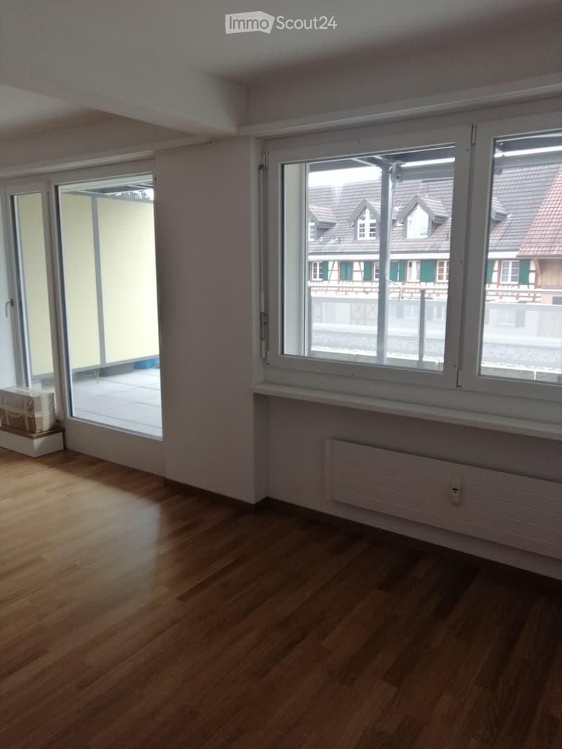 Empty room with wooden flooring, large windows, and a sliding door leading to a balcony.