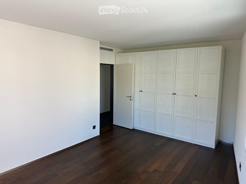 Empty room with light-colored walls, dark wooden flooring, and built-in white wardrobes.