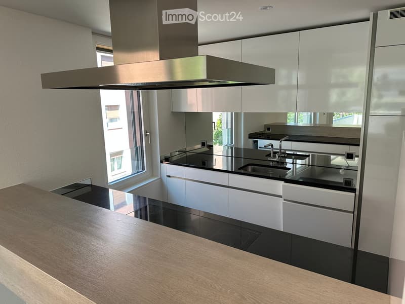 Modern kitchen with white cabinets, black countertops, stainless steel sink, and a range hood above.