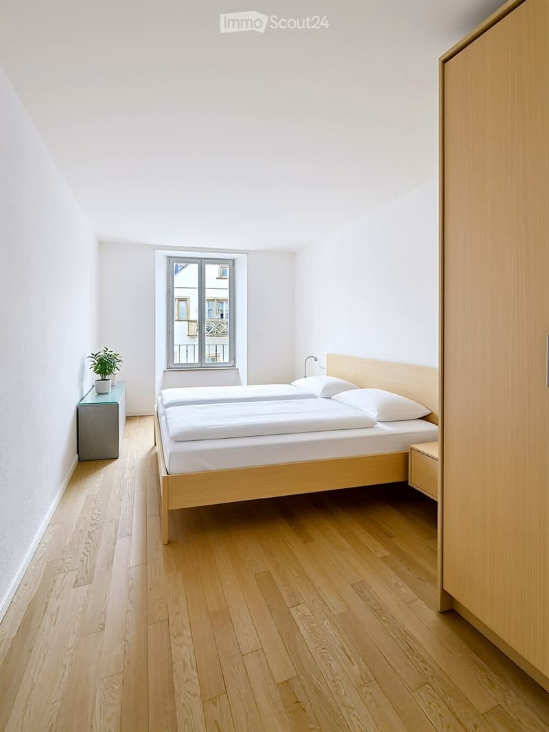 Minimalist bedroom with a wooden bed, white bedding, a small nightstand with a plant, and a built-in wardrobe.
