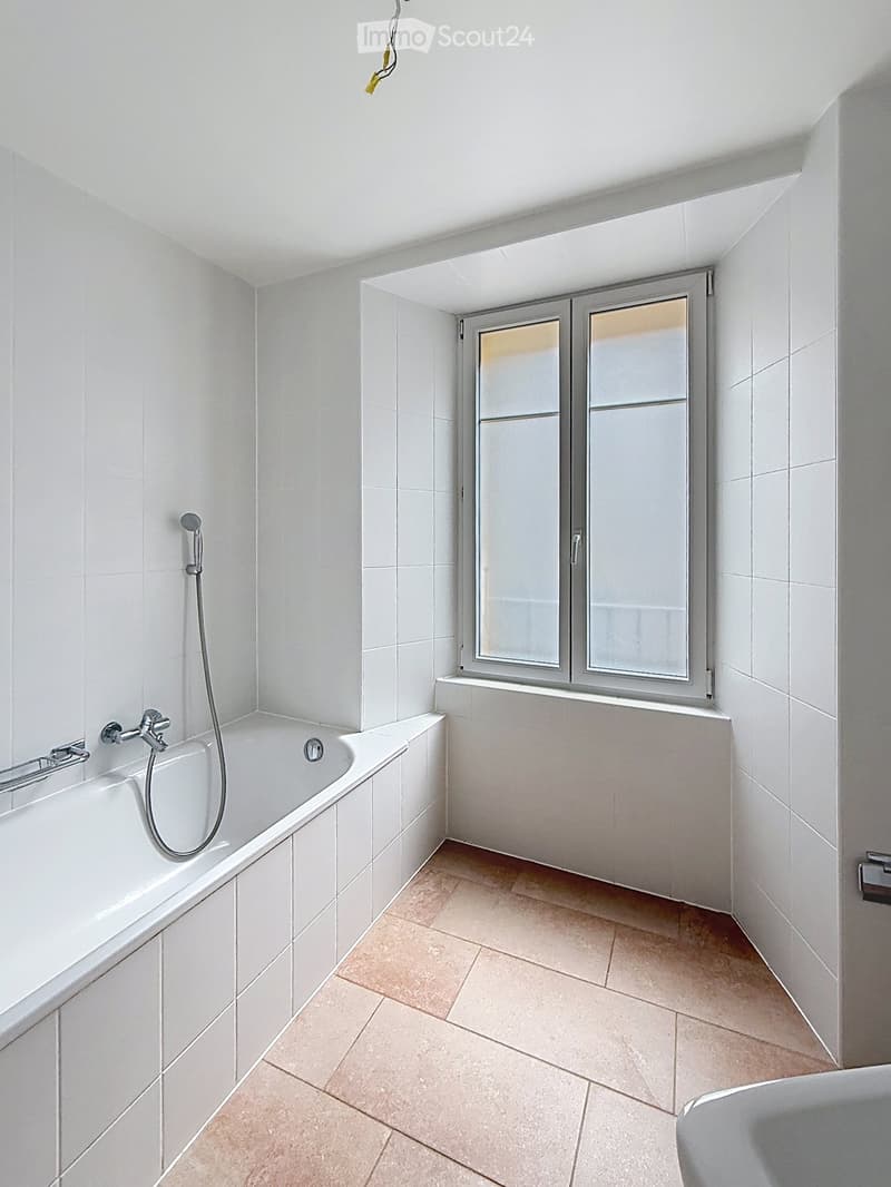 Modern bathroom with white tiled walls, a bathtub, a showerhead, and a window with frosted glass panels.