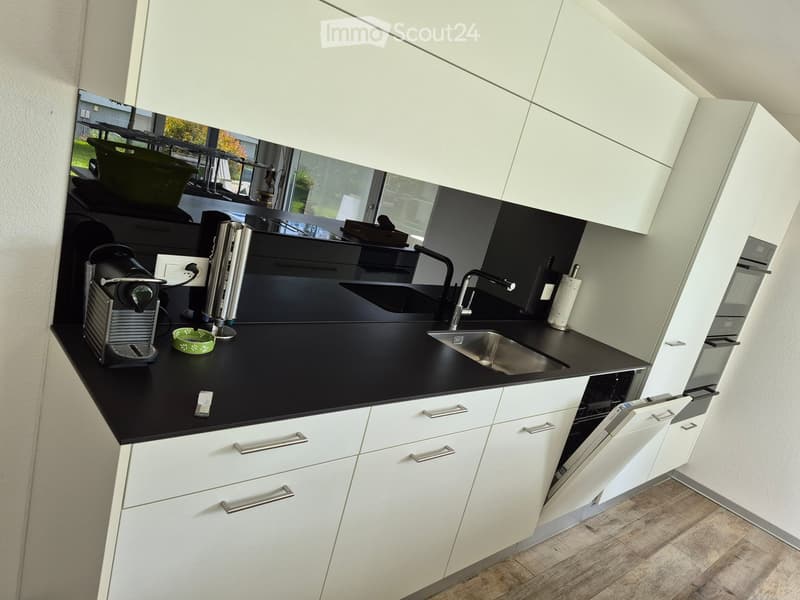 Modern kitchen with white cabinets, black countertops, stainless steel sink, and a coffee maker on the counter.