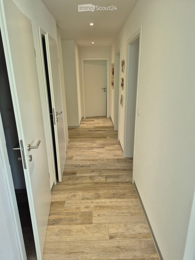 Clean, modern hallway with light wooden flooring, white walls, and several doors leading to different rooms.