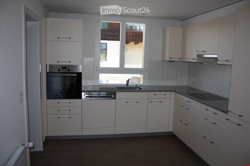 Modern kitchen with white cabinets, stainless steel appliances, granite countertops, and a window overlooking a neighboring building.
