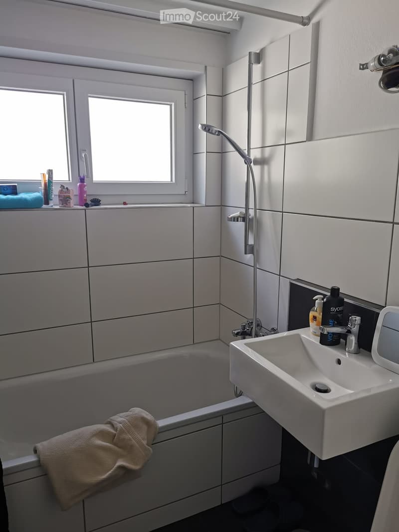 Modern bathroom with a bathtub, sink, showerhead, and various toiletries on the windowsill and sink counter.