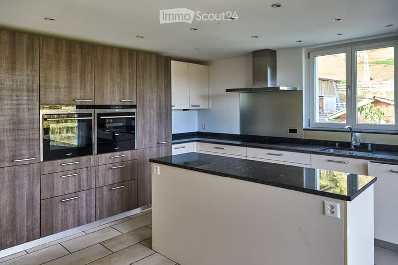 Modern kitchen with dark countertops, light-colored cabinets, stainless steel appliances, and a central island.