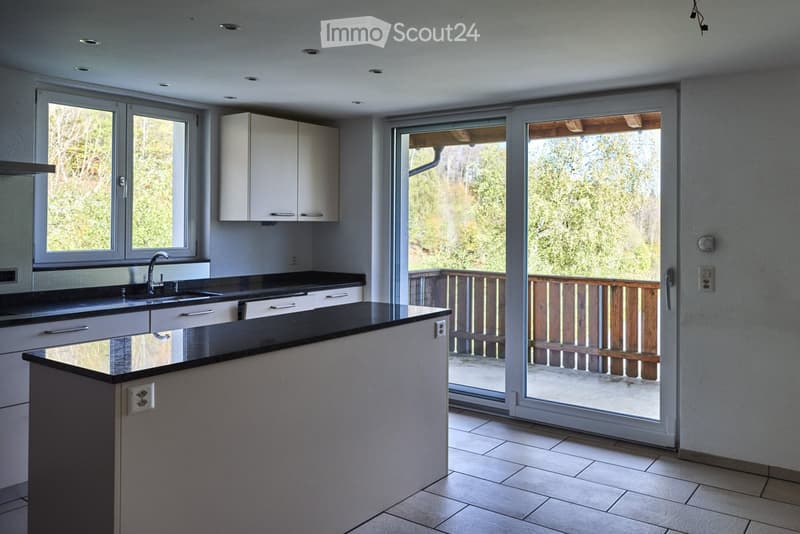 Modern kitchen with white cabinets, black countertops, and a central island. Large windows and sliding glass doors open to a wooden balcony.