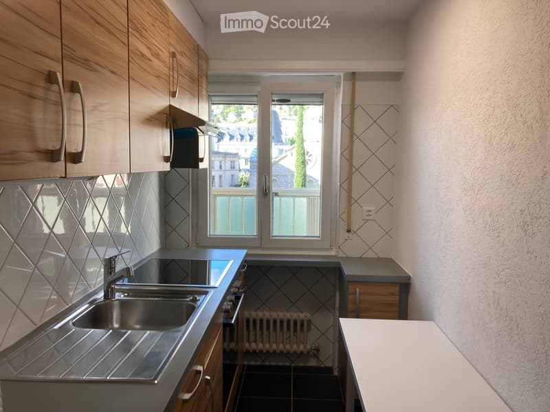 Modern kitchen with wooden cabinets, stainless steel sink, and tiled backsplash. Features a window with a view of the street and a radiator below.