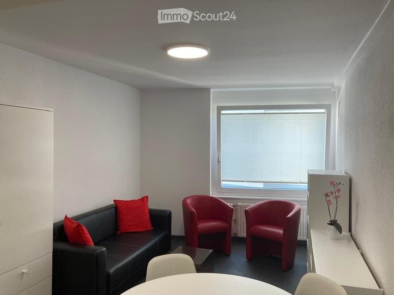 Modern living room with a black leather sofa, red throw pillows, red armchairs, a white coffee table, and a small white side table with a flower pot.