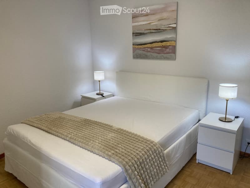 A modern bedroom with a neatly made bed, two nightstands with table lamps, and a large abstract painting on the wall.