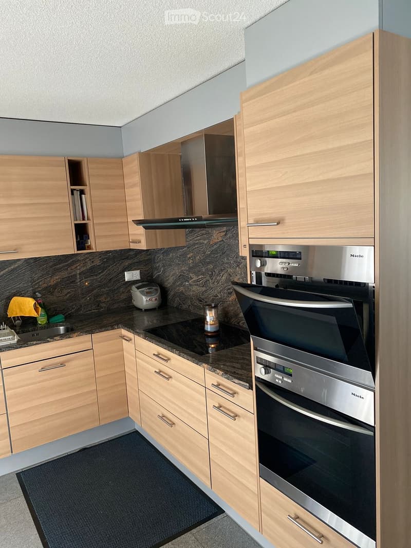 Modern kitchen with light wooden cabinets, stainless steel appliances, granite countertop, and a built-in oven.