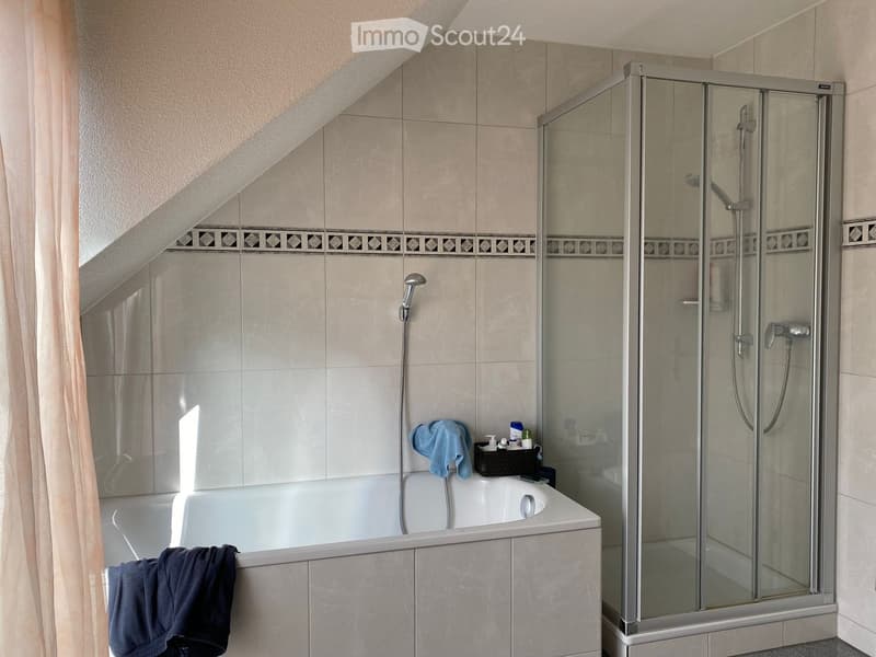 Bathroom with a bathtub, glass-enclosed shower, tiled walls, and towels on the edge of the tub.