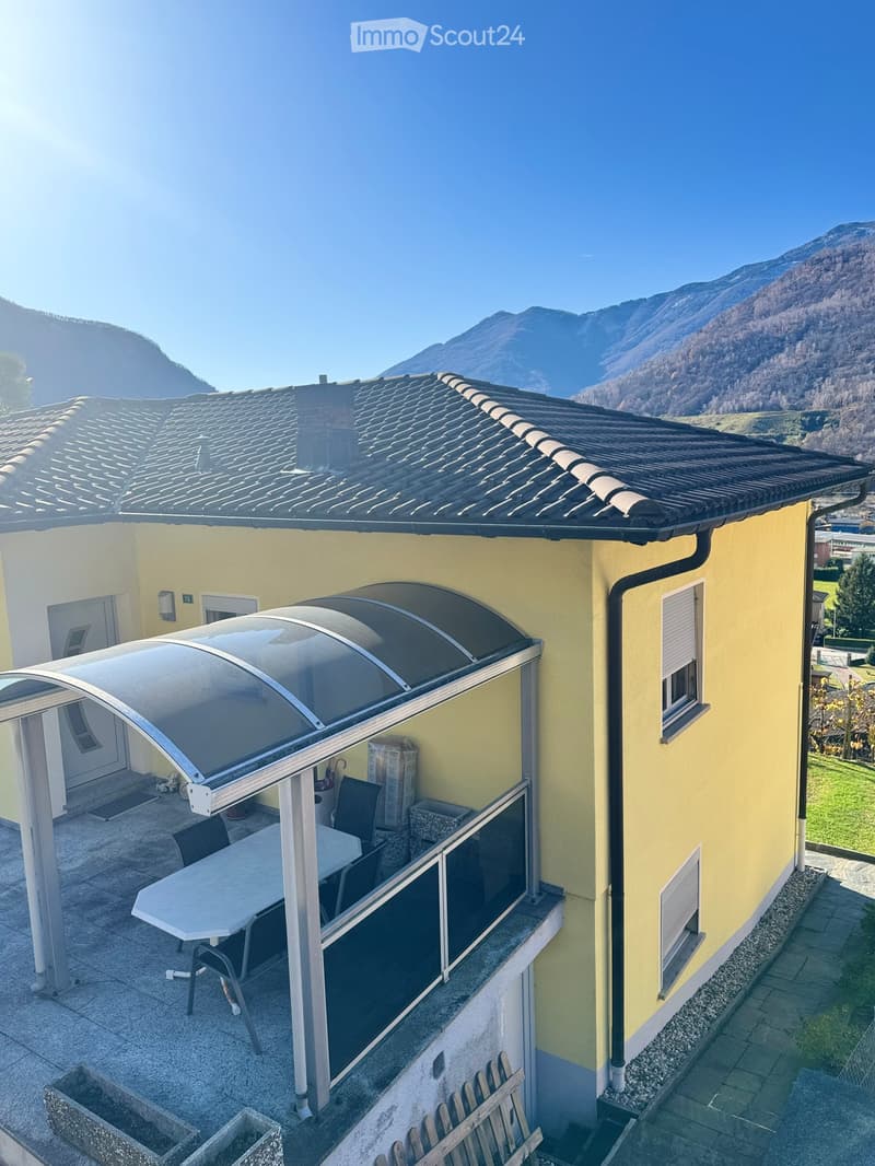 Balcony with a retractable awning, table, chairs, and a scenic mountain view.