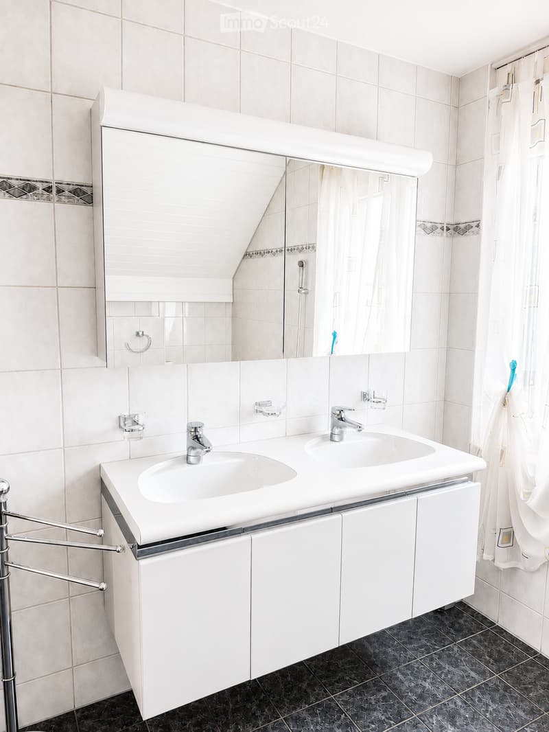 Modern bathroom with white tiles, double sink vanity, large mirror, towel rack, and dark tiled floor.