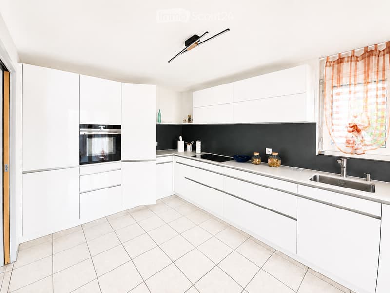 Modern kitchen with white cabinets, stainless steel appliances, and a black backsplash. Features an oven, sink, countertop, and various small decorative items.