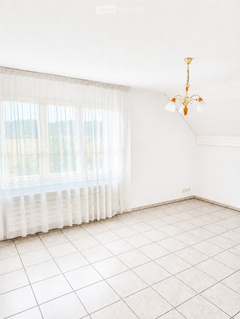 Empty room with white tiled flooring, white walls, large windows with sheer curtains, and a decorative chandelier.