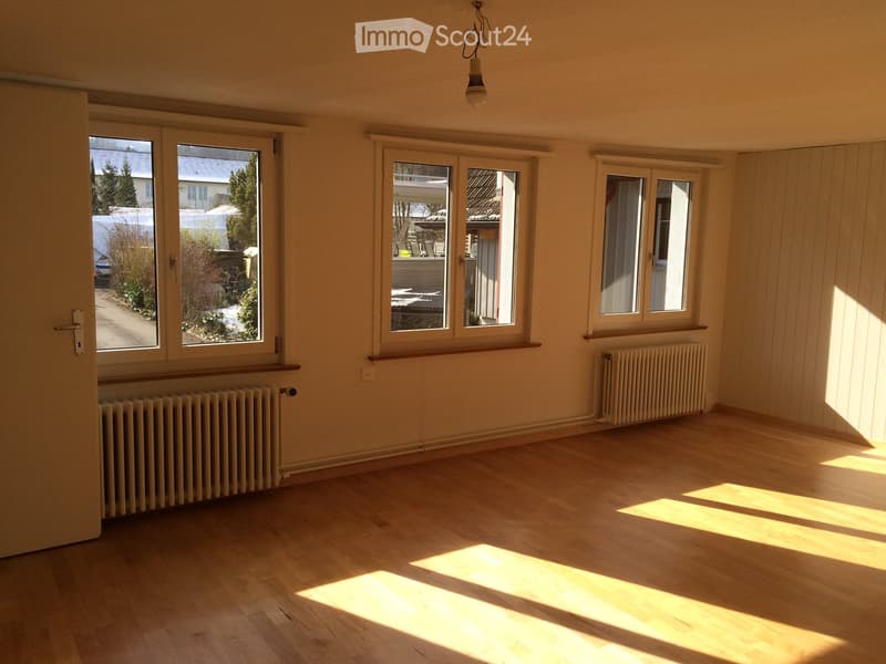 Empty room with wooden flooring, large windows, radiators, and natural light streaming in.