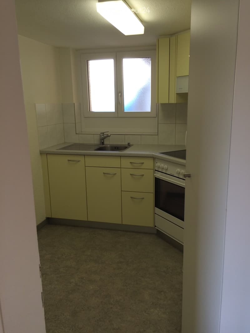 Empty kitchen with light-colored cabinets, a sink, and an oven. The space has tiled walls and a window above the sink.