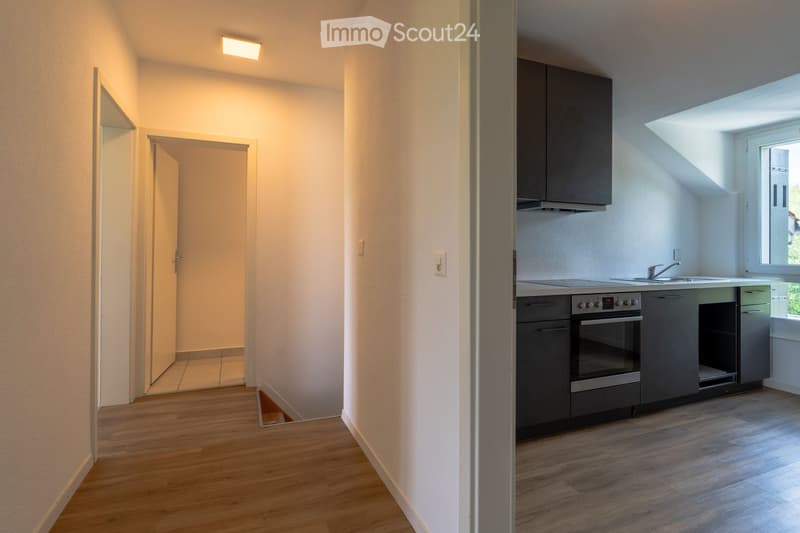 Modern kitchen with wooden flooring, grey cabinets, built-in oven, sink, and faucet. The space is bright with natural light from a window and has a sleek, contemporary design.